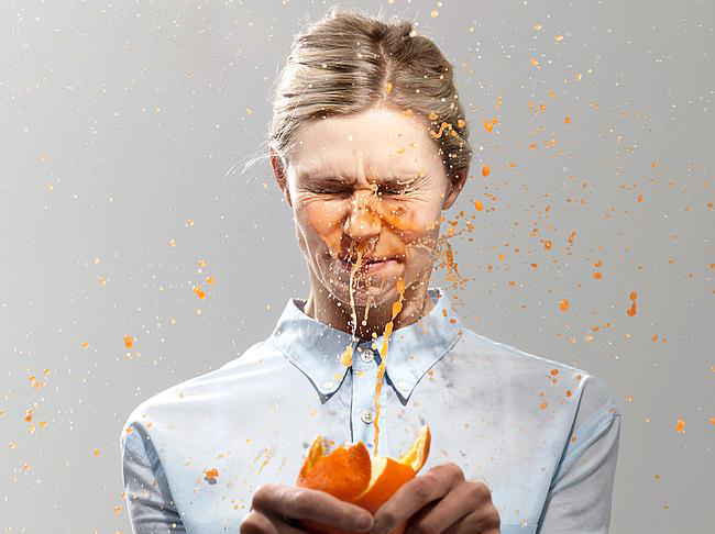 Woman splashed with juice from orange, studio shot